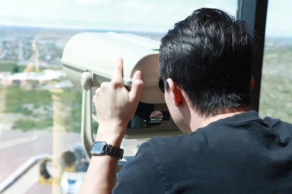 Man looking through a coin operated Tower Viewer or Stationary Binoculars a top of a building
