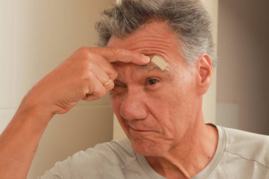 Yarasını sarmak için bir adamın alnına yara bandı yapıştırdım.