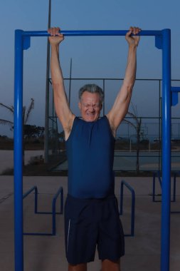 Yaşlı Olgun Adam açık hava fitness parkında çekme çubuğundan sarkıyor ve geriyor.