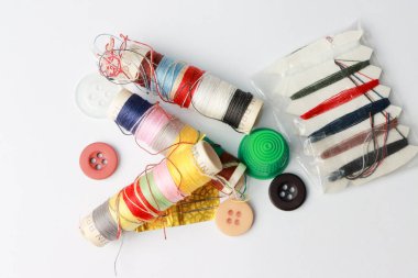 Beyaz zemin üzerinde farklı renk iplik ve iğne makaraları, yüksük ve düğmeler ile seyahat seti