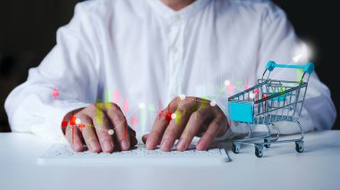 İş adamı pazarlama grafiğini teknolojiyle, alışveriş arabasıyla ve klavyeyle analiz ediyor..