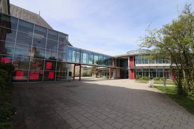 HAAG, GERMANY - 20 Nisan 2025: Oberbayern 'deki Realschule Haag' ın iki binasını birbirine bağlayan cam kaplı yaya köprüsü, kırmızı yapısal unsurlar tarafından desteklenmektedir. Yüksek kalite fotoğraf