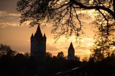 HAAG, GERMANY - 14 Mayıs 2013: Schlossturm ve Kleiner Schlossturm in Haag in Oberbayern 'in günbatımı, ağaç dalları tarafından çerçevelenmiş canlı turuncu ve sarı bir gökyüzüne karşı siluet. Yüksek kalite fotoğraf