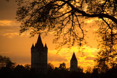 HAAG, GERMANY - 14 Mayıs 2013: Schlossturm ve Kleiner Schlossturm in Haag in Oberbayern 'in günbatımı, ağaç dalları tarafından çerçevelenmiş canlı turuncu ve sarı bir gökyüzüne karşı siluet. Yüksek kalite fotoğraf