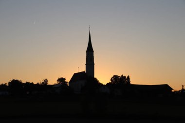 SoYEN, ALMANY - 13 Mayıs 2025: Soyen yakınlarındaki Katolik Kilisesi Mariae Himmelfahrt, günbatımına karşı güzel bir şekilde siluetlendi, tarihi mimarisini ve manevi önemini vurguladı. Yüksek kalite