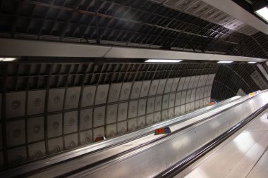 LONDON, UNITED KINGDOM - 23 Aralık 2017: Londra metro istasyonunun içinde metalik paneller, floresan aydınlatma ve duvarlar boyunca mimari simetri içeren yürüyen merdiven tüneli