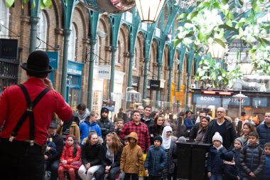 Londra, UNITED KINGDOM - 30 Aralık 2017: Bir sokak sanatçısı melon şapkalı ve kırmızı askılı tarihi Covent Garden Market 'in içinde aile ve turistler bir araya toplanırken,