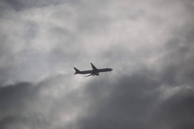 LONDON, UNITED KINGDOM - 30 Aralık 2017: Londra üzerinde gündüz vakti bulutlu bir gökyüzünde uçan ticari uçak, dramatik bulutlu hava koşullarına karşı siluetlendi. Yüksek kalite fotoğraf