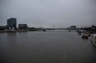 COLOGNE, GERMANY - 29 Aralık 2017: Kasvetli bir kış gökyüzü altında, her iki kıyıya demirli tekneler ve modern binalar ile Ren Nehri aşağı bakan bulutlu manzara. Yüksek kalite