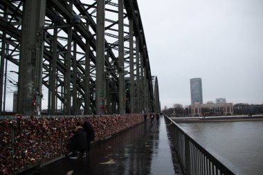 COLOGNE, GERMANY - 29 Aralık 2017: Yağmurlu bir kış gününde aşk kilitleriyle kaplı Hohenzollern Köprüsü, Ren Nehri ve bulutlu bir gökyüzünün altında şehir manzarası. Yüksek kalite fotoğraf