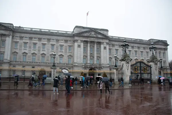 LONDON, UNITED KINGDOM - 23 ARALIK 2017: Şemsiyeli turistler yağmurlu bir kış günü Londra 'daki Buckingham Sarayı' nın dışında toplanarak, yağmurlu asfaltın önündeki ıslak zeminde yansımalar görülebilir.