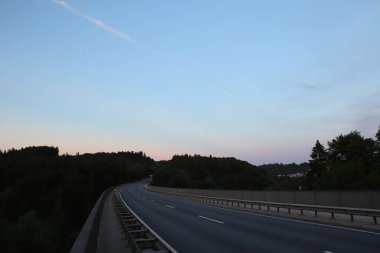 WASSERBURG AM Hanı, ALMANY - 19 Mayıs 2025: Orman manzarası boyunca ilerleyen Innbruecke köprüsünün sakin akşam sahnesi günbatımında açık bir gökyüzü. Yüksek kalite fotoğraf