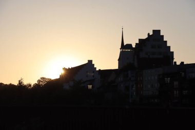 WASSERBURG AM Hanı, ALMANY - 30 Mayıs 2025: Burg Wasserburg kalesinin siluetli manzarası ve arka planda sıcak turuncu gökyüzü olan tarihi binalar. Yüksek kalite fotoğraf
