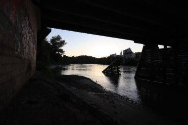 WASSERBURG AM Hanı, GERMANY - 30 Mayıs 2025: Köprü sütununda grafiti ile Innbruecke 'nin altından akşam görüntüsü, siluetli buz kırıcı yapılar, ve Burg Wasserburg' ün tarihi silueti