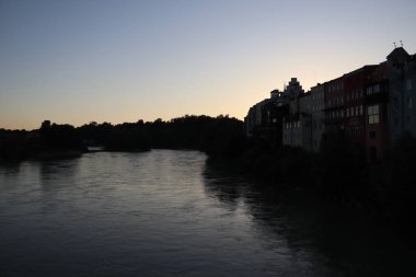 ChatGPT: WASSERBURG AM INN, GERMANY - 30 Mayıs 2025: Innbruecke Köprüsü 'nden batıya bakan akşam manzaralı Innbruecke Nehri üzerinde şehrin ufuk çizgisi ve günbatımının suya yansıması. Yüksek kalite fotoğraf