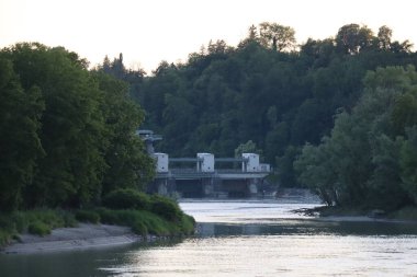 WASSERBURG AM Hanı, ALMANY - 30 Mayıs 2025: Innbruecke Köprüsü 'nden Innbruecke Hanının üzerindeki ağaçlar tarafından çerçevelenmiş Wasserkraftwerk Wasserburg hidroelektrik santralinin uzak görüntüsü. Yüksek kalite fotoğraf