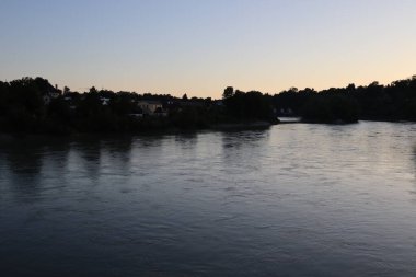 ChatGPT: WASSERBURG AM INN, GERMANY - 30 Mayıs 2025: Innbruecke Köprüsü 'nden batıya bakan akşam manzaralı Innbruecke Nehri üzerinde şehrin ufuk çizgisi ve günbatımının suya yansıması. Yüksek kalite fotoğraf
