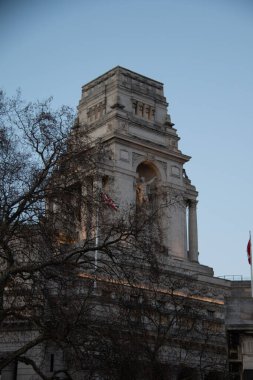 LONDON, UNITED KINGDOM - 1 HAZİRAN 2018: Trinity Meydanı 'ndaki tarihi Londra Liman Binası' nın kulesi, ön planda açık gökyüzü ve kış ağaçlarıyla sokak seviyesinden görüldü. Yüksek