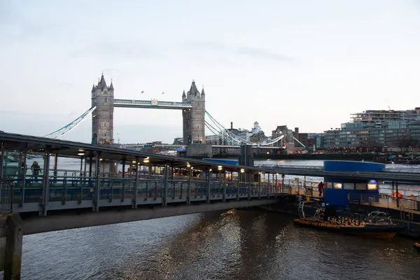 LONDON, UNITED KINGDOM - 1 HAZİRAN 2018: Thames Nehri üzerinde yansımaları olan nehir kenarındaki bir gezinti alanından Tower Bridge 'in gündüz görüşü ve ön plandaki modern yürüme yolları. Yüksek kalite fotoğraf