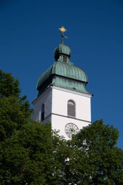 EBERSBERG, GERMANY - 8 Mayıs 2018: Ebersberg, Bavyera 'da açık mavi bir gökyüzü altında yeşil ağaçların üzerinde yükselen Maria Hüküm Kilisesi' nin çan kulesinin dikey görüntüsü. Yüksek kalite fotoğraf
