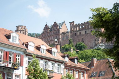 HeideELBERG, ALMANY - 19 Mayıs 2018: Heidelberg Şatosu 'nun ön planda ağaçlar ve tarihi binalarla birlikte eski kasabanın çatılarından yükselen manzarası. Yüksek kalite fotoğraf