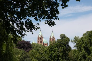 SPEYER, ALMANY - 21 Mayıs 2018: Güneşli bir günde yemyeşil ağaçlar ve mavi gökyüzü tarafından çerçevelenmiş Speyer Katedrali 'nin uzak görüntüsü. Yüksek kalite fotoğraf