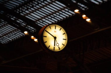 LEIPZIG, ALMANY - 18 Ağustos 2018: akşam saatlerinde Leipzig Hauptbahnhof merkez tren istasyonunun içindeki çatıdan sarkan aydınlanmış istasyon saati. Yüksek kalite fotoğraf