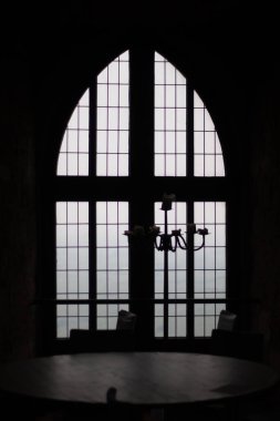 Büyük kemerli katedral penceresinin önünde, şebeke camları ve gün ışığıyla asılı duran siluetli avize. Yüksek kalite fotoğraf