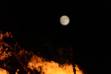  Gece ve ışıkta, uzak bir şenlik ateşinin üzerinde parlak ay. Yüksek kalite fotoğraf