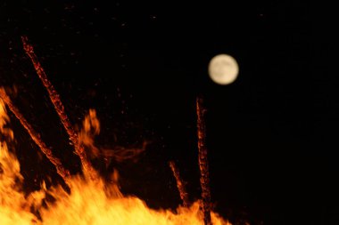  Geceleyin parlak turuncu alevlerle dolu büyük bir şenlik ateşinin üzerinde dolunay. Yüksek kalite fotoğraf