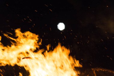  Geceleyin parlak turuncu alevlerle dolu büyük bir şenlik ateşinin üzerinde dolunay. Yüksek kalite fotoğraf