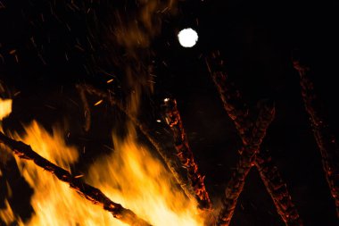  Geceleyin parlak turuncu alevlerle dolu büyük bir şenlik ateşinin üzerinde dolunay. Yüksek kalite fotoğraf