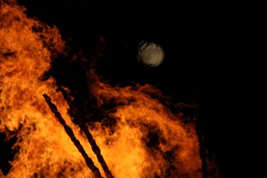  Geceleyin parlak turuncu alevlerle dolu büyük bir şenlik ateşinin üzerinde dolunay. Yüksek kalite fotoğraf