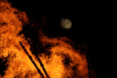  Geceleyin parlak turuncu alevlerle dolu büyük bir şenlik ateşinin üzerinde dolunay. Yüksek kalite fotoğraf