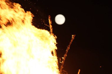  Geceleyin parlak turuncu alevlerle dolu büyük bir şenlik ateşinin üzerinde dolunay. Yüksek kalite fotoğraf