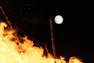  Geceleyin parlak turuncu alevlerle dolu büyük bir şenlik ateşinin üzerinde dolunay. Yüksek kalite fotoğraf