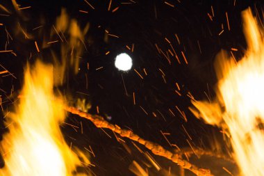  Geceleyin parlak turuncu alevlerle dolu büyük bir şenlik ateşinin üzerinde dolunay. Yüksek kalite fotoğraf