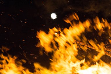  Geceleyin parlak turuncu alevlerle dolu büyük bir şenlik ateşinin üzerinde dolunay. Yüksek kalite fotoğraf