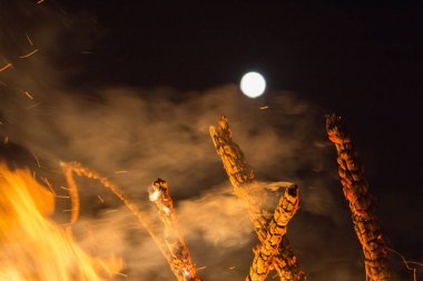  Geceleyin parlak turuncu alevlerle dolu büyük bir şenlik ateşinin üzerinde dolunay. Yüksek kalite fotoğraf