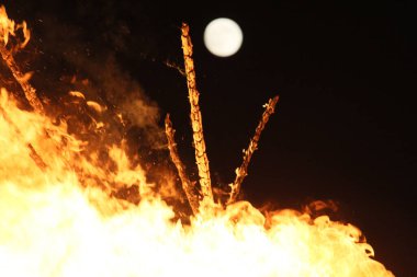  Geceleyin parlak turuncu alevlerle dolu büyük bir şenlik ateşinin üzerinde dolunay. Yüksek kalite fotoğraf