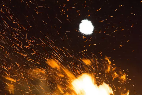  Geceleyin parlak turuncu alevlerle dolu büyük bir şenlik ateşinin üzerinde dolunay. Yüksek kalite fotoğraf