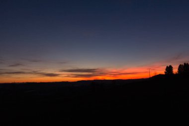 Akşamları parlak turuncu ve mavi gökyüzü gradyanı olan karanlık bir arazide gün batımı. Yüksek kalite fotoğraf