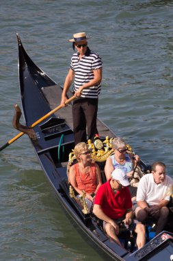Venedik, İtalya - 24 AĞUSTOS 2013: Turistler Venedik 'teki Büyük Kanal' da çizgili tişörtlü bir gondolcu tarafından yönetilen bir gondola biniyor. Yüksek kalite fotoğraf