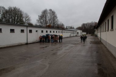 DACHAU, GERMANY - 25 Kasım 2017: Ziyaretçiler Dachau toplama kampı anısına yağmurlu bir günde tarihi kışla alanından geçerek yürüyorlar. Yüksek kalite fotoğraf