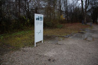 DACHAU, GERMANY - 25, 2017 NOVEMBER: Ağaçlarla çevrili çakıl yolu boyunca yerleştirilmiş Dachau toplama kampı anıtının site haritası ile açık hava bilgi panosu. Yüksek kalite fotoğraf