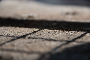 Metal bir çitin gölgesi yumuşak bir odak noktasında güneş ışığıyla aydınlatılmış bir kaya zemin yüzeyine düşüyor. Yüksek kalite fotoğraf