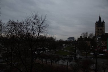 COLOGNE, ALMANY - 29 ARALIK 2017 Köln 'de bulutlu bir gökyüzüne karşı gölgelenmiş Büyük St. Martin Kilisesi ve yakındaki park ağaçlarının alacakaranlık manzarası. Yüksek kalite fotoğraf