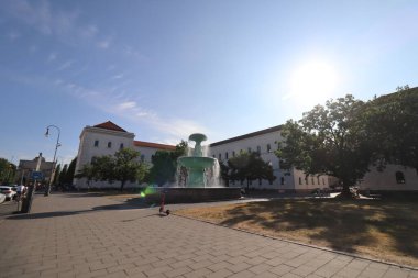 MUNİK, GERMANY - 24 Haziran 2025: İnsanlar arka planda fıskiye, güneş ışığı ve tarihi binalarla Profesör-Huber-Platz 'dan geçiyorlar. Yüksek kalite fotoğraf