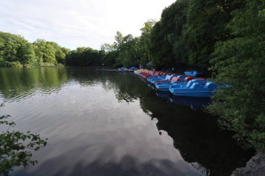 MUNICH, Almanya - 24 Haziran 2025: Suya yansıyan yemyeşil ağaçlarla çevrili sakin bir nehre yanaşmış pedal botlar. Yüksek kalite fotoğraf