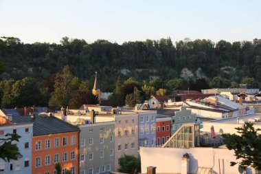 WASSERBURG AM Hanı, GERMANY - 20 Haziran 2025: Wasserburg am Inn 'deki tarihi binalar ve çatılar, arka planda ormanlık bir tepe ile sıcak akşam güneşi ışığı altında. Yüksek kalite
